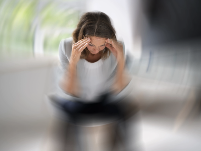 Psychiatrie Eine Frau fasst sich an die Stirn, alles dreht sich um sie herum.