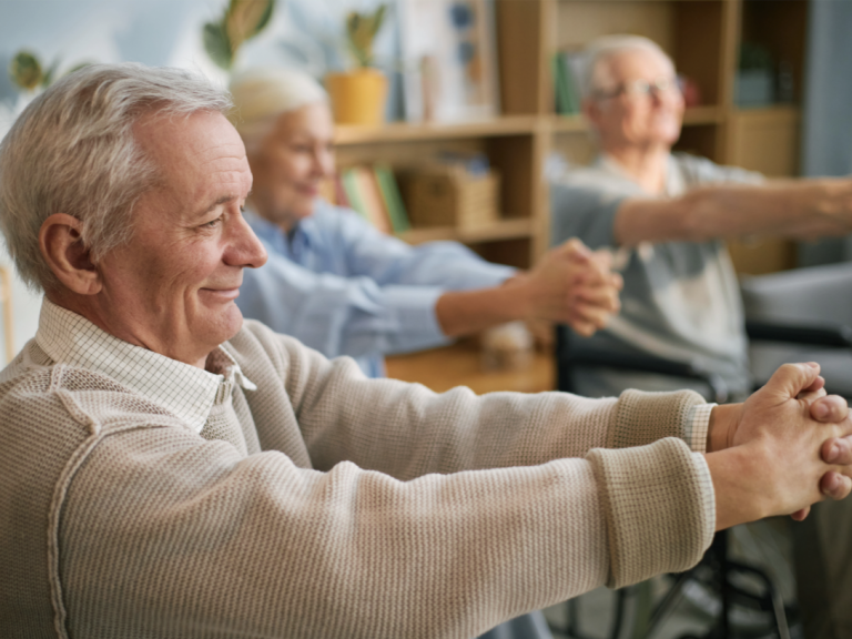 Geriatrie Drei ältere Menschen heben die Arme, die Finger sind verschränkt, sie lächeln.